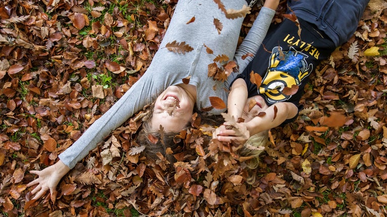 Two children laughing as they roll in dry oak leaves